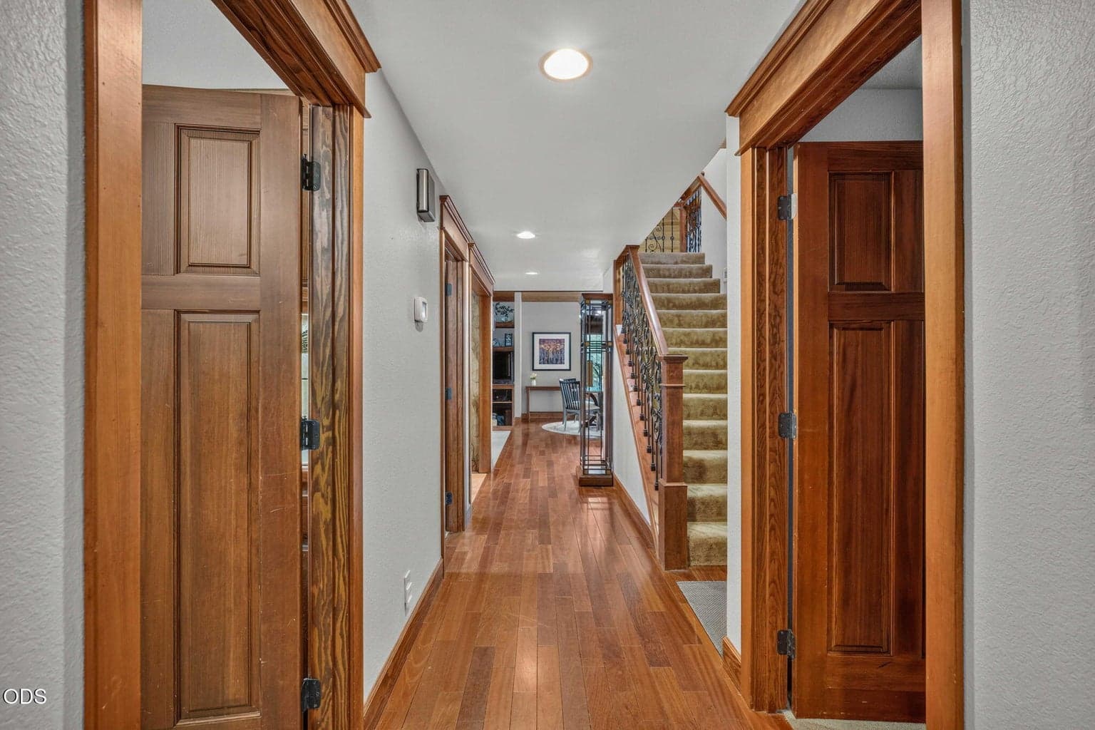 Warm wood trim and floors lead through the main hall toward open living and dining spaces.