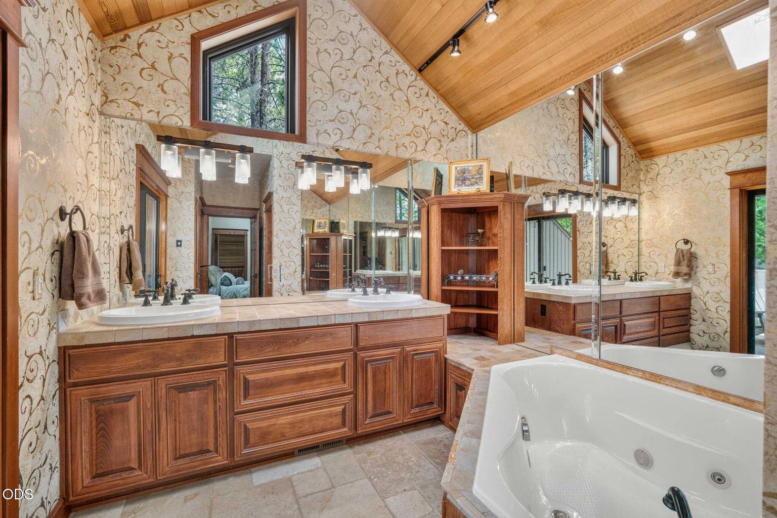 Vaulted ensuite bath with double vanity, heated travertine tile and jetted tub under skylight and custom story window.