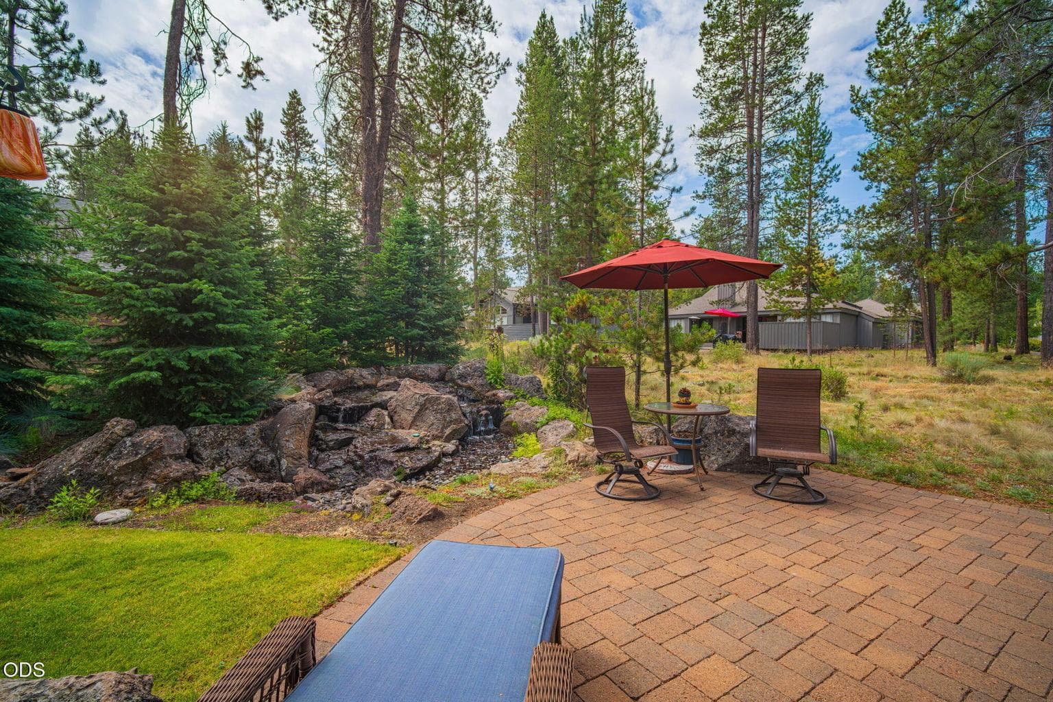 Professionally landscaped backyard with dense evergreens, along the grassy lawn, provides a band of privacy and a lovely setting with sounds from the water feature.