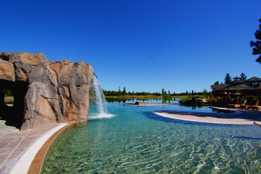 Located at the edge of an expansive lake, the pool decks and swimming pool merge with the shoreline of the lake creating an “infinity” edge. Faux boulders reinforce the illusion that the pool and lake are a single body of water, and also form “grotto” areas for hot tubs. “Lava tube” tunnels and a slide with waterfall provide enjoyable areas for children to explore in a lively family atmosphere. Expansive glass opens the exercise rooms up to the views of the lake and surrounding mountains.