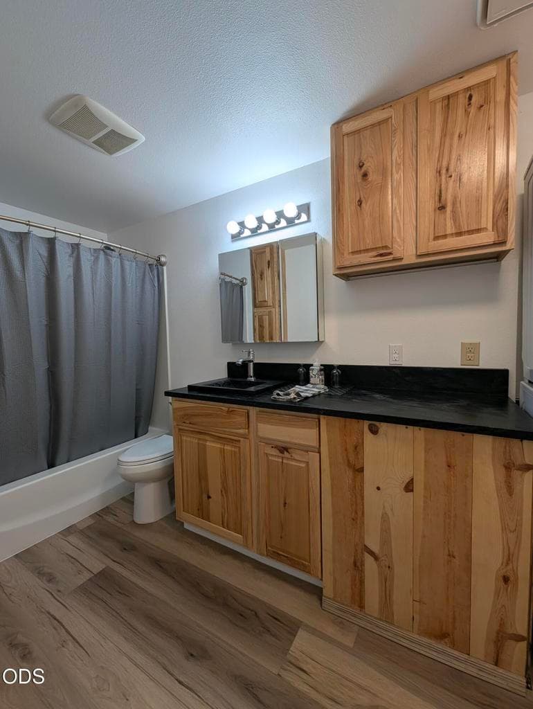 Bathroom vanity area with wood cabinetry, dark countertop, updated flooring, and modern fixtures.