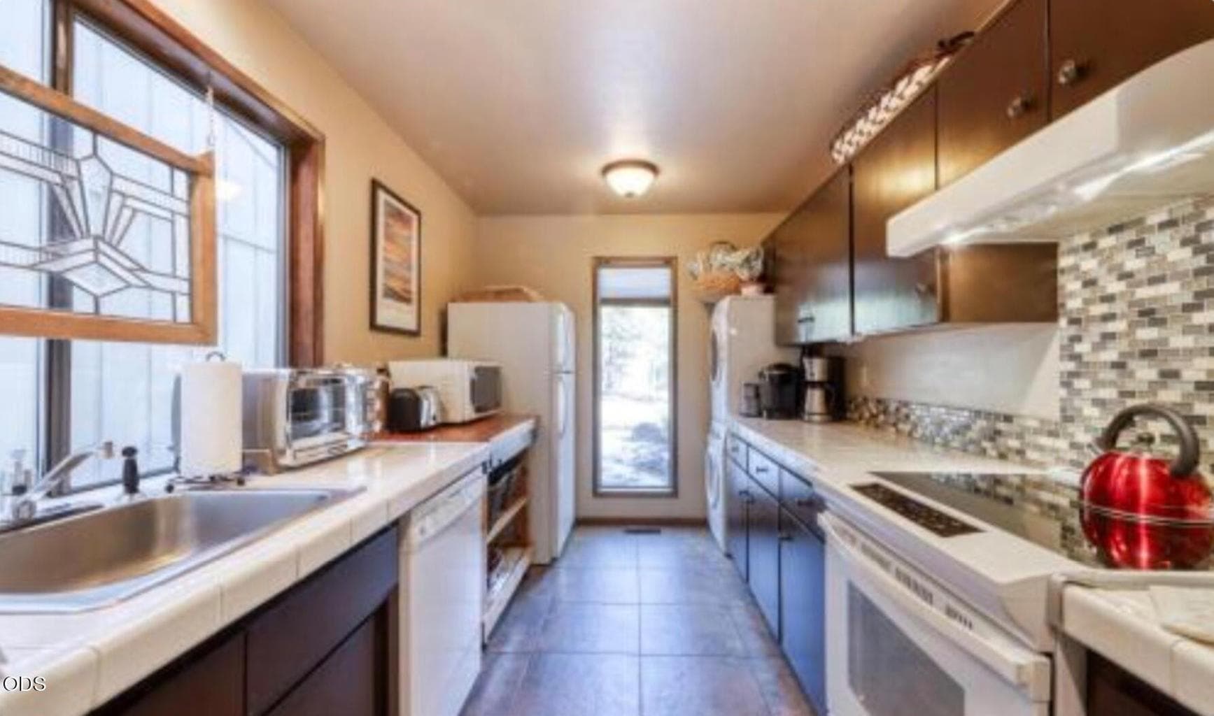 Efficient galley kitchen with tile flooring, generous counter space, updated backsplash, and convenient laundry area nearby for everyday functionality.
