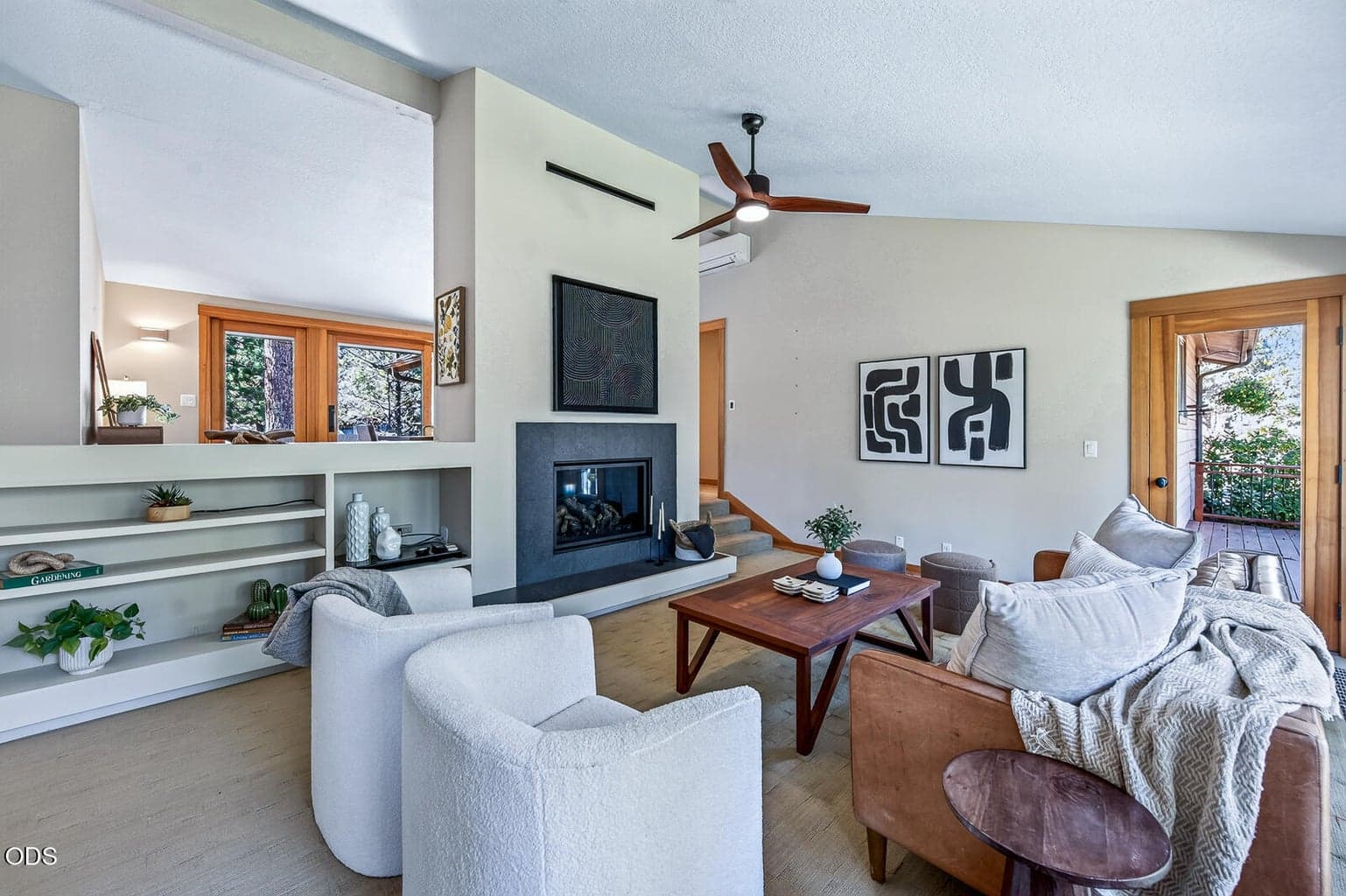 Spacious living room with tall ceilings and a propane fireplace. This view is from the front door. The dining room is beyond the fireplace. A deck through the door to the right.