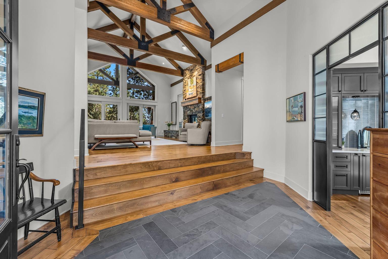 A dramatic entry with slate and hickory hardwood flooring opens to soaring ceilings and exposed timber trusses, while steel and glass doors to the right reveal a versatile wine or game room.