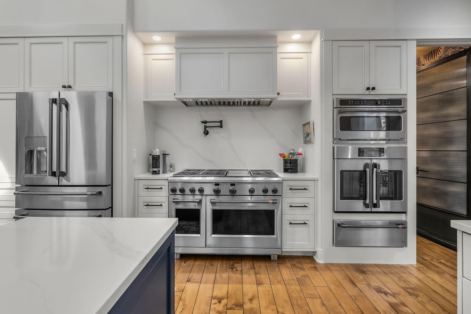 Professional-grade range framed by clean-lined cabinetry, with discreet access to an expansive butler’s pantry offering extended prep space, storage, and additional refrigeration.