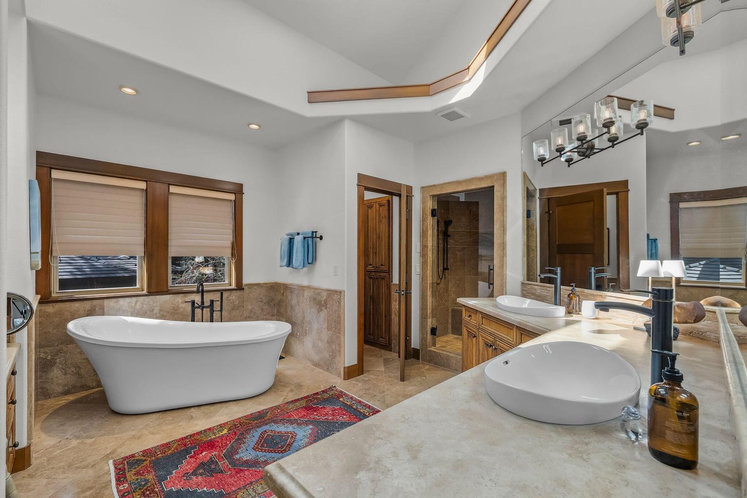 Well-appointed primary bath with soaking tub, dual vanities, walk-in shower, and layered natural finishes creating a calm, refined feel.