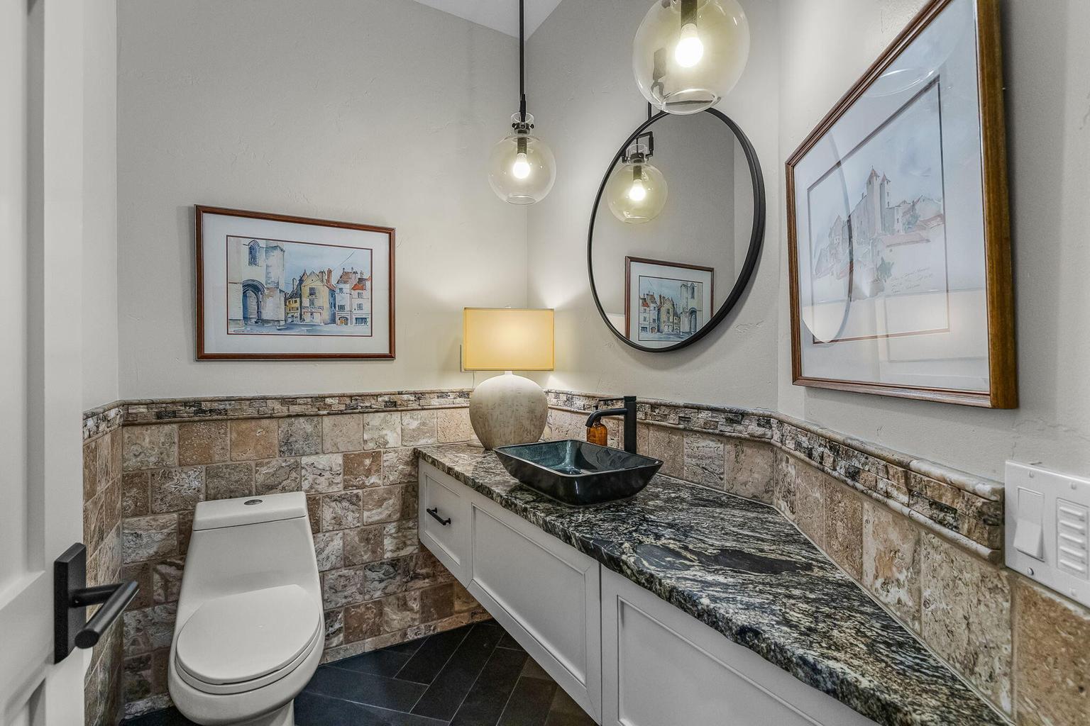 Privately located powder room featuring stone finishes, a vessel sink, and designer lighting.