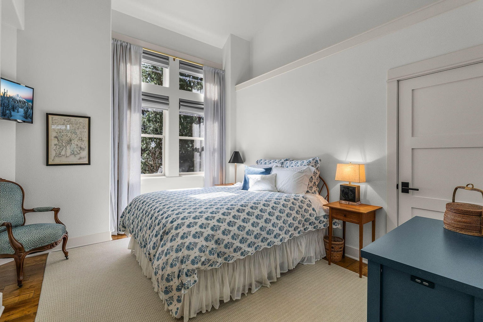 Light-filled en-suite guest bedroom set within the guest wing of the home, featuring tall windows, vaulted ceiling, and a quiet, private setting.