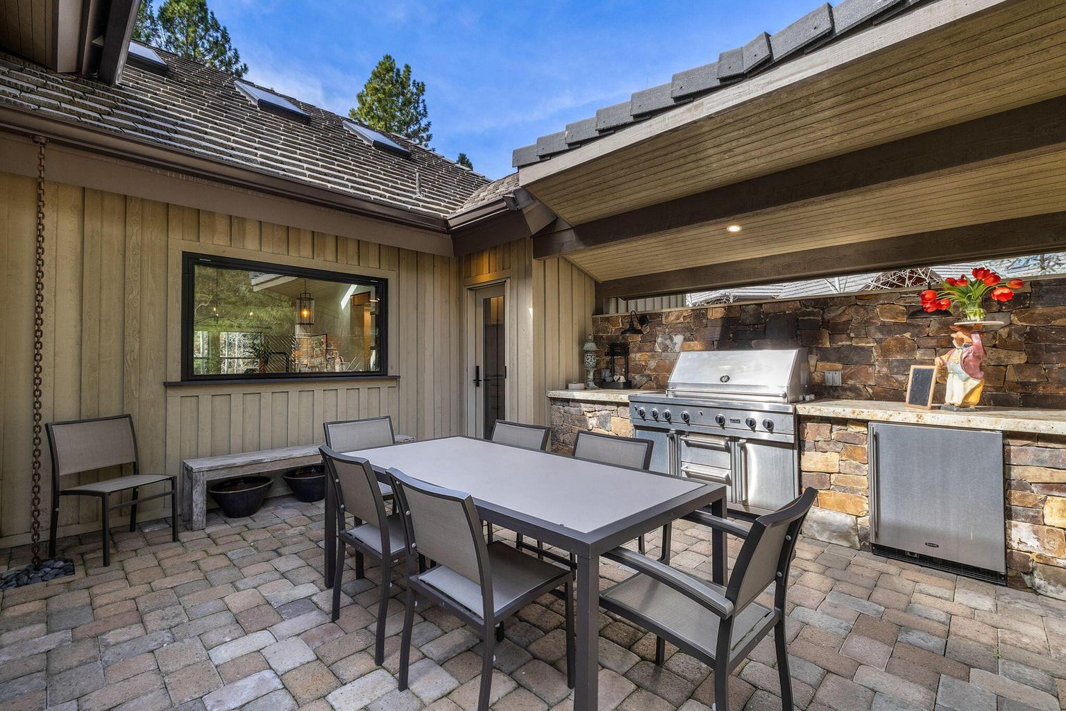 Well-appointed outdoor kitchen and dining area with built-in grill, stone finishes, and a pass-through window from the kitchen for easy indoor-outdoor connection.