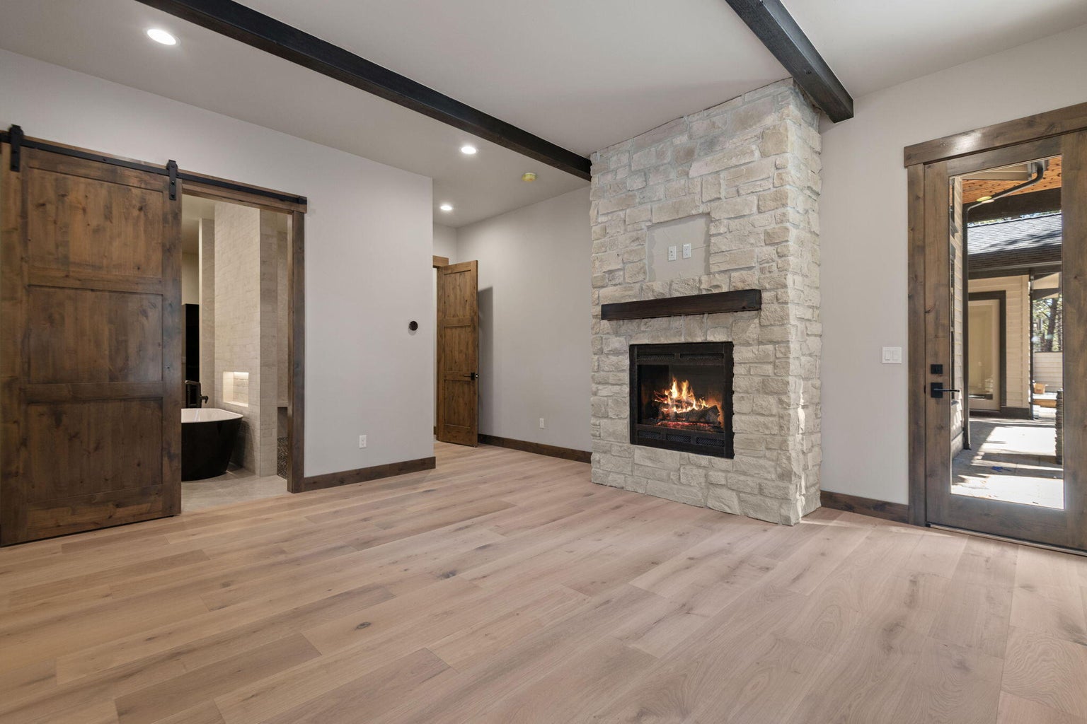 Main level Primary with bath ensuite with custom barn door, custom beamed ceiling, rocked gas fireplace, and entry to exterior and patio