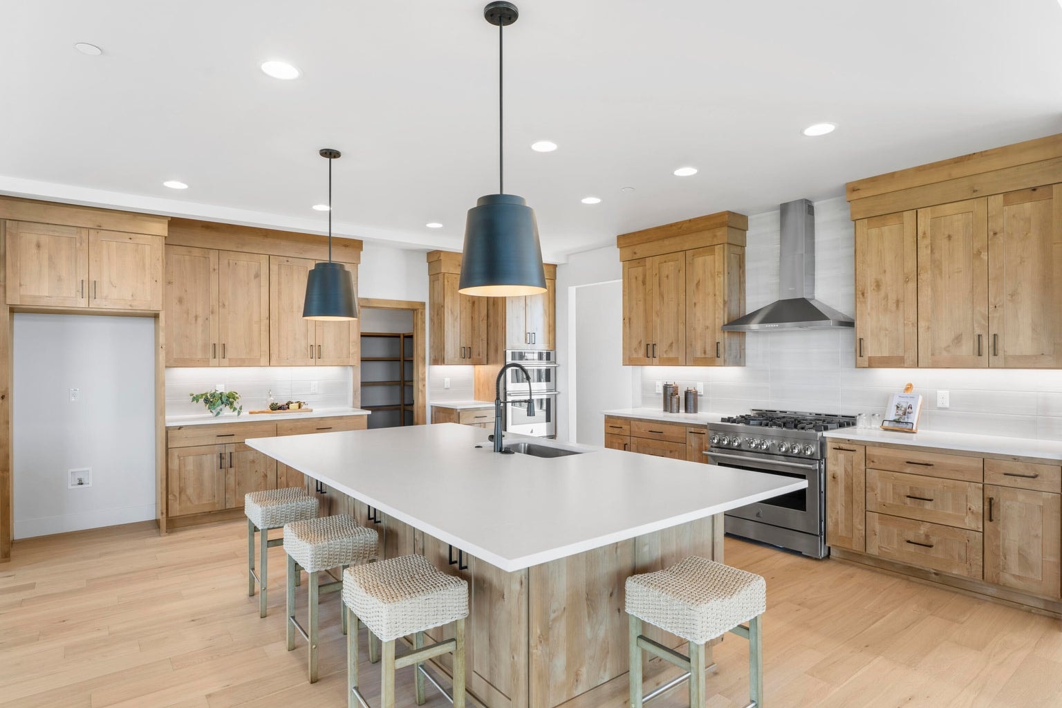The kitchen features an oversized island and spacious work areas. The gas range and hood are separate from an oven and microwave