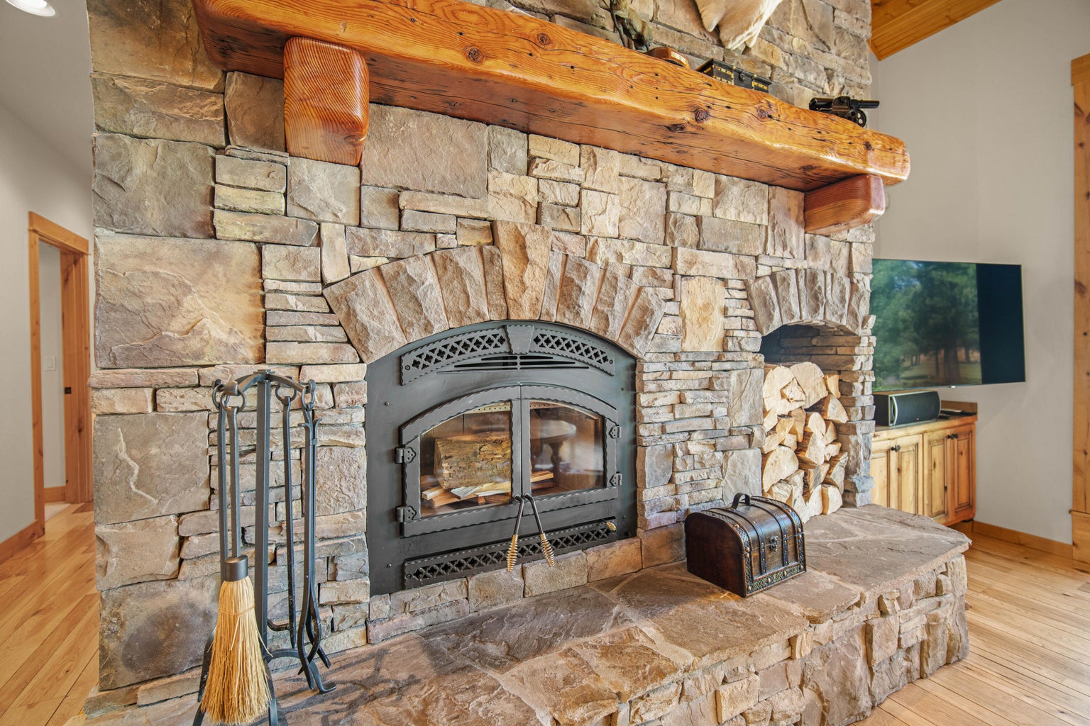Close-up of the substantial stone fireplace with wood mantel, hearth, firewood storage, and rustic design details.