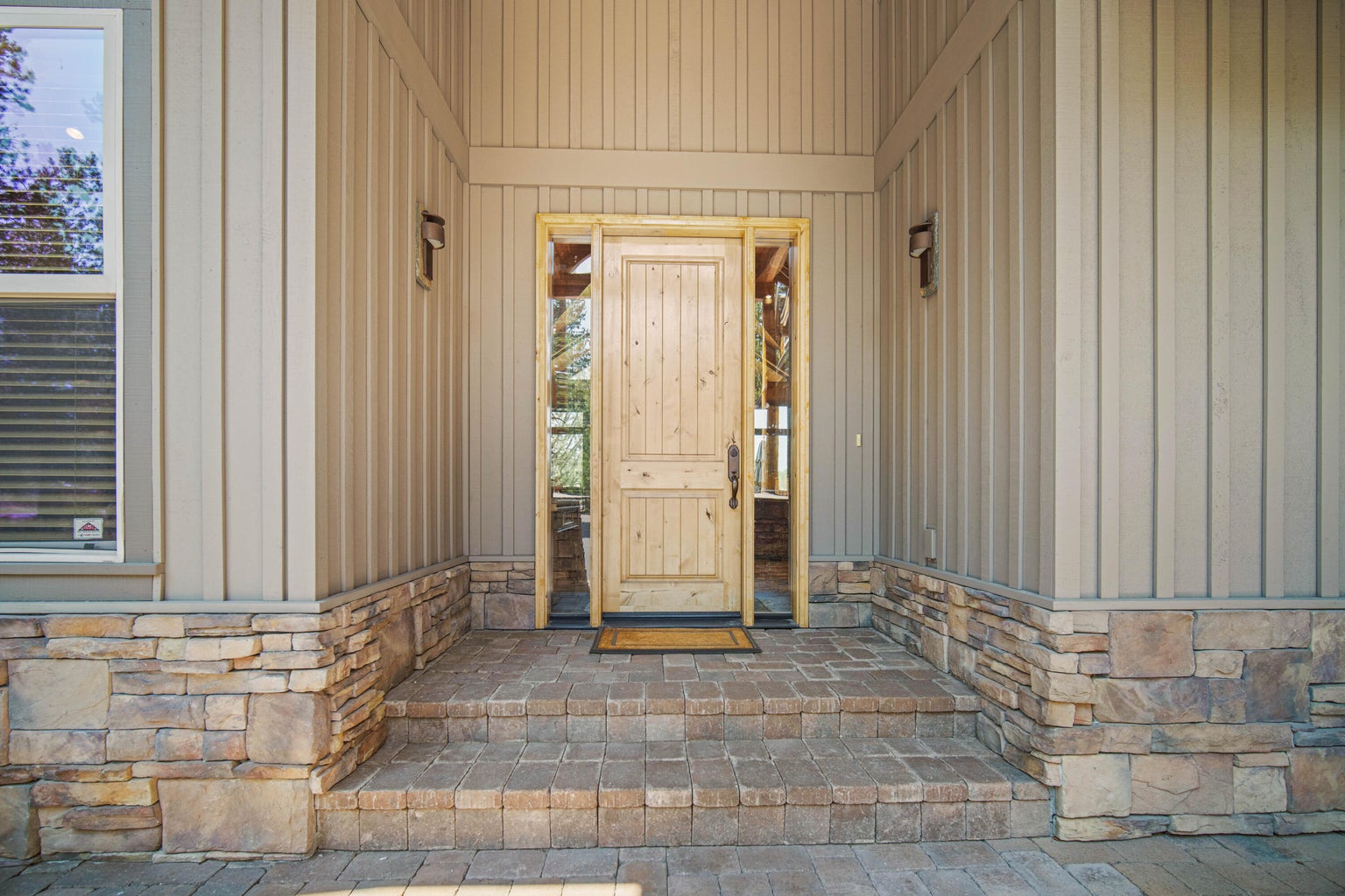 Covered front entry with stonework, paver steps, natural wood door, and warm lodge-inspired details.