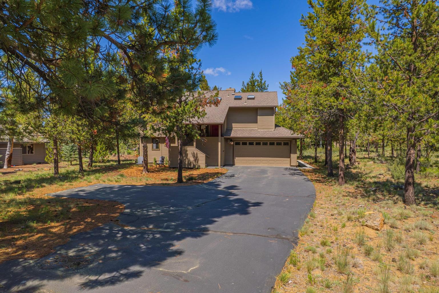 Front exterior view with attached two-car garage, paved driveway, and natural Central Oregon landscaping.