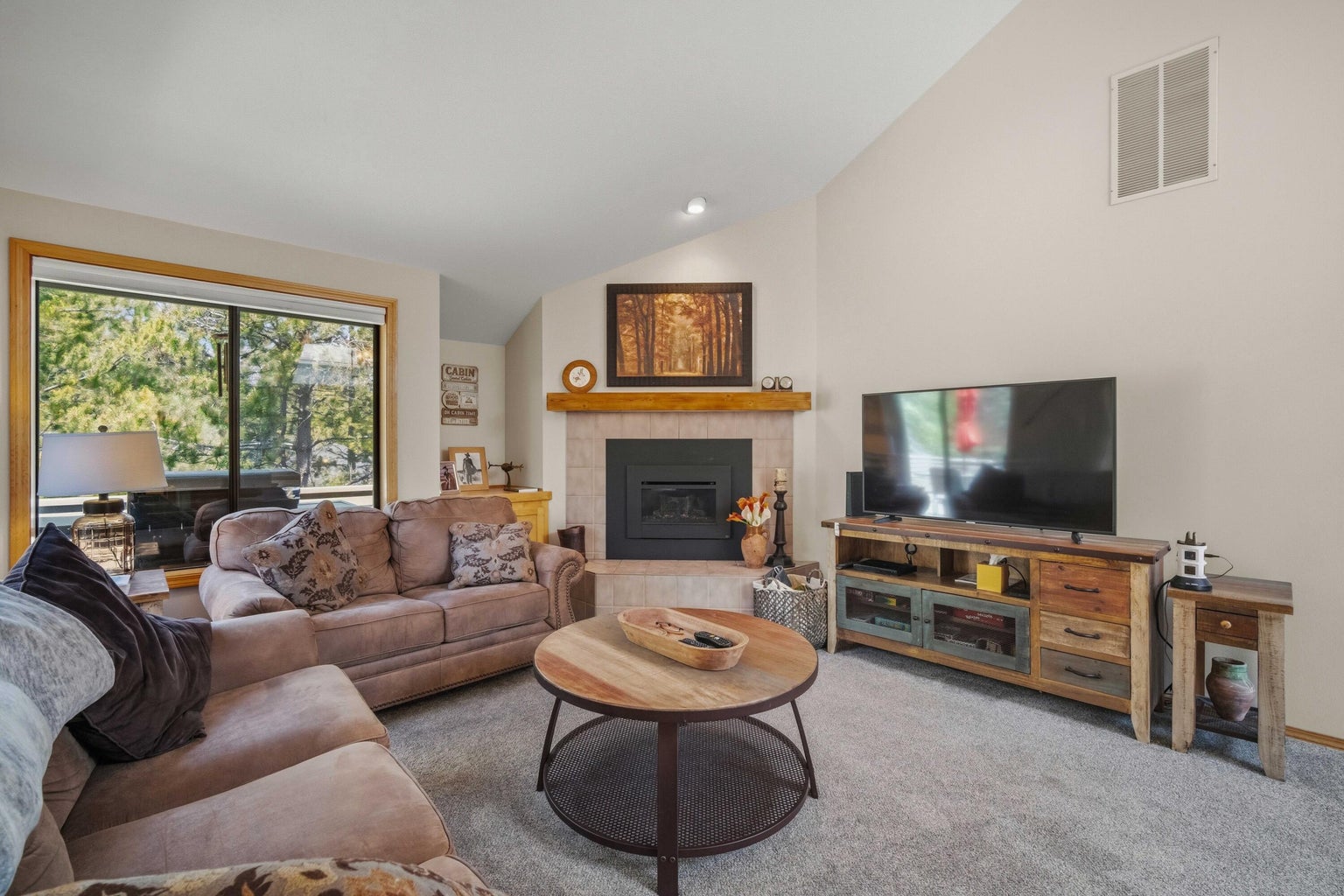 Comfortable living room with fireplace focal point, tree views, and bright neutral finishes.