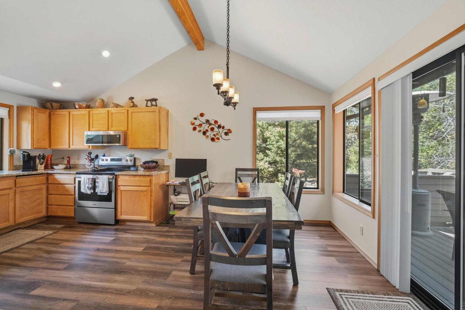 Dining area with vaulted ceiling, updated flooring, and large windows overlooking the trees.