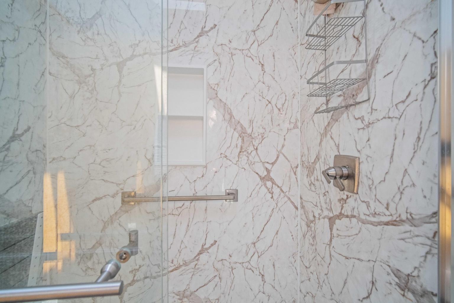 Updated primary walk-in shower with glass door and marble-look surround.