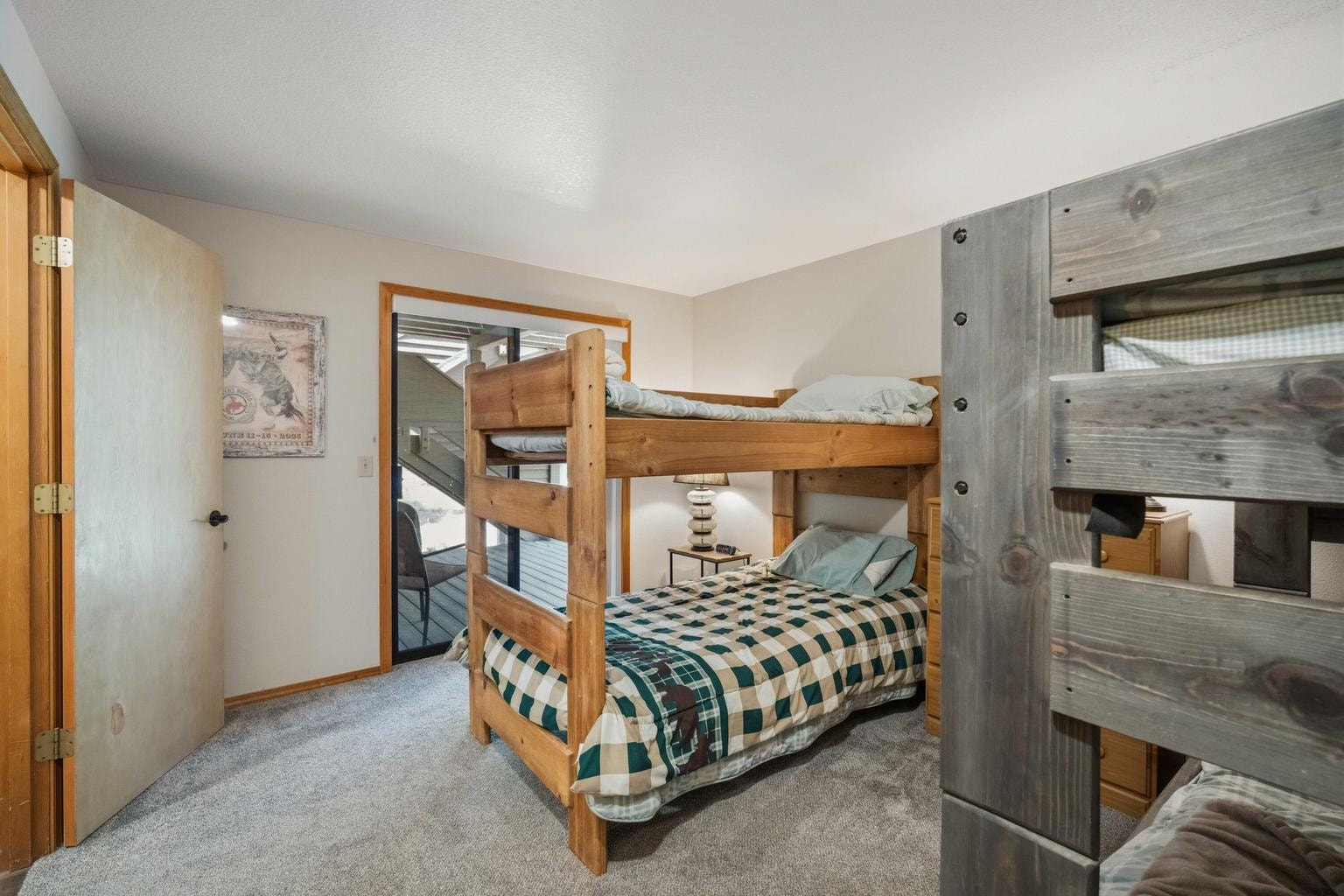 Bunk room with sliding door to the covered lower deck and wooded setting.