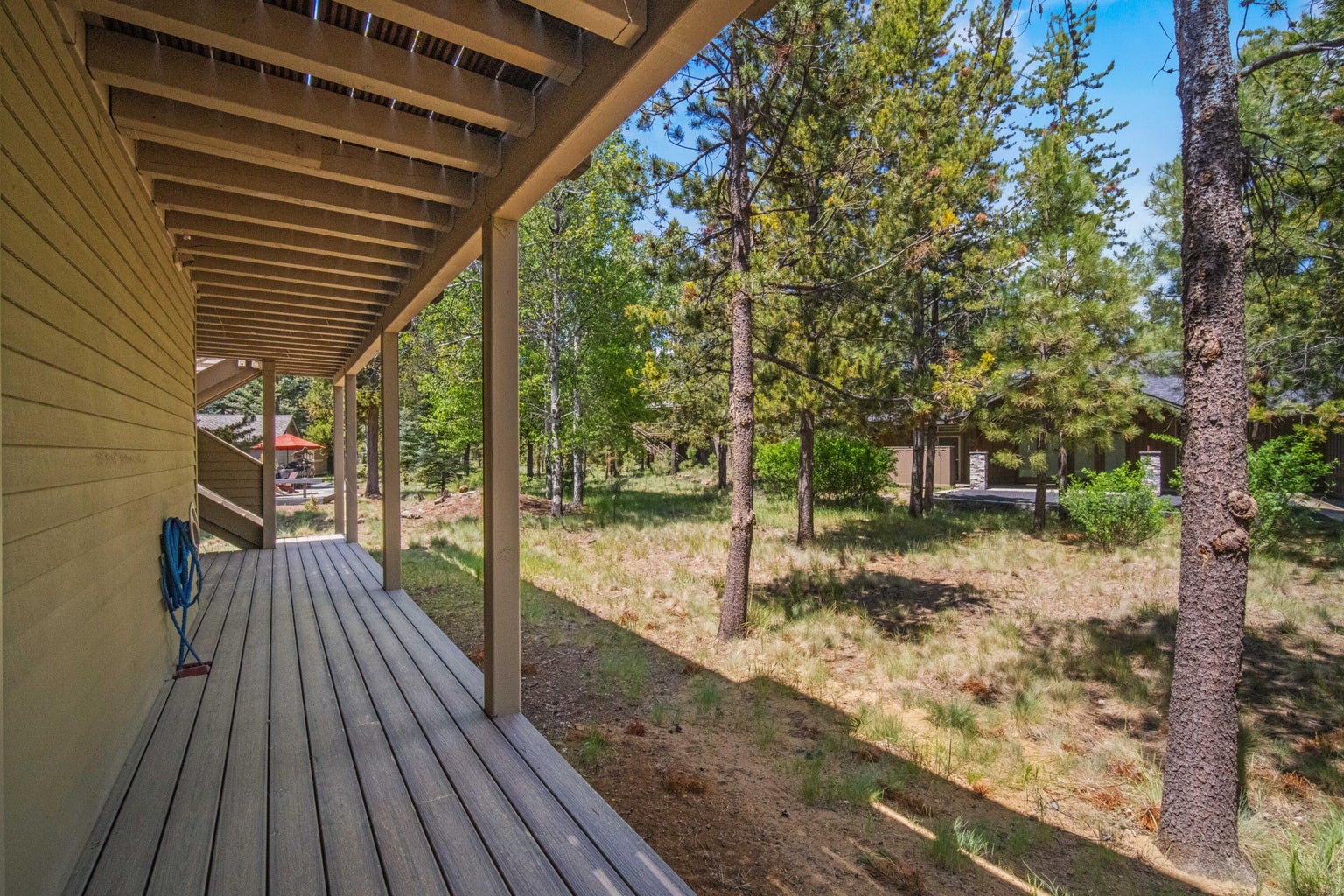 Rear exterior view showing the elevated upper deck, lower covered patio, and natural lot.