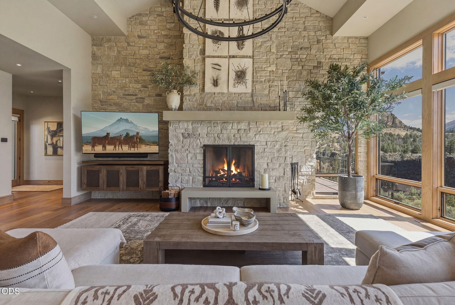 Living room, stone fireplace lit, vaulted ceiling, canyon views through floor-to-ceiling windows