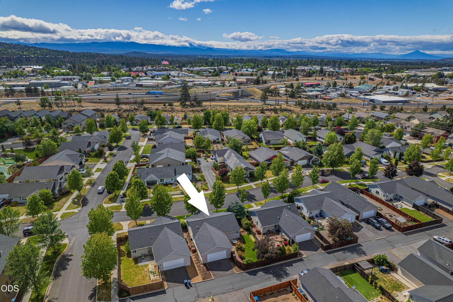 A wider aerial showcases the home’s Bend location with neighborhood streets, nearby services, and Central Oregon scenery beyond.