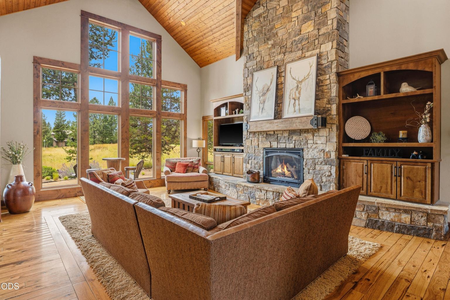 The dramatic great room showcases soaring tongue-and-groove ceilings, a floor-to-ceiling stone fireplace, and expansive windows that frame the views.