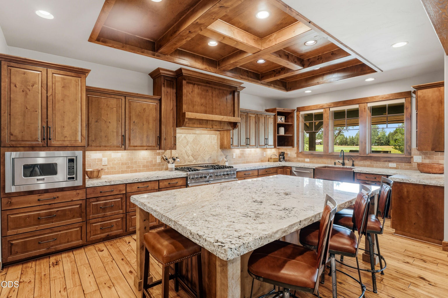 A spacious granite island with seating, coffered wood ceiling, and abundant custom cabinetry creates the perfect gathering space for family and friends.