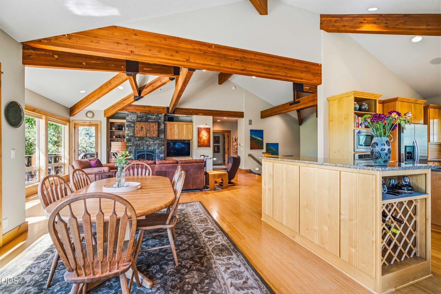 An expansive open living area introduces the warmth and scale of this Sunforest-built Sunriver home, with exposed wood beams, bamboo flooring, a stone fireplace, dining space and kitchen connected beneath a dramatic vaulted ceiling.