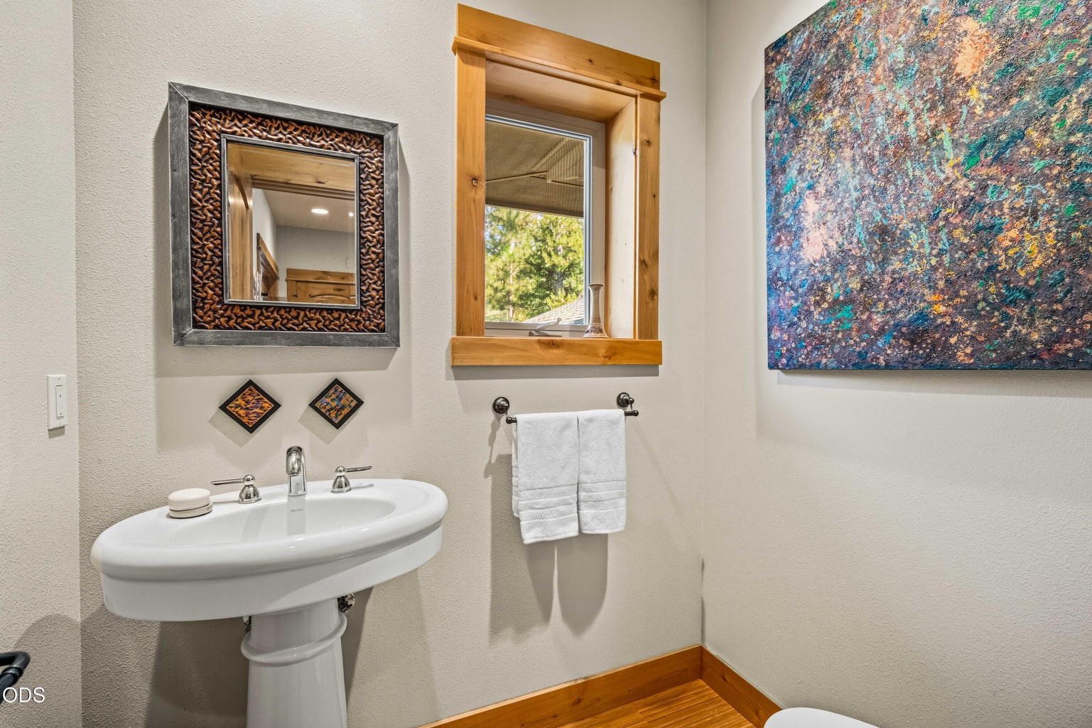 The upper-level powder room is thoughtfully finished with a pedestal sink, custom wood trim, natural light and artful details convenient to the great room, dining area and kitchen.