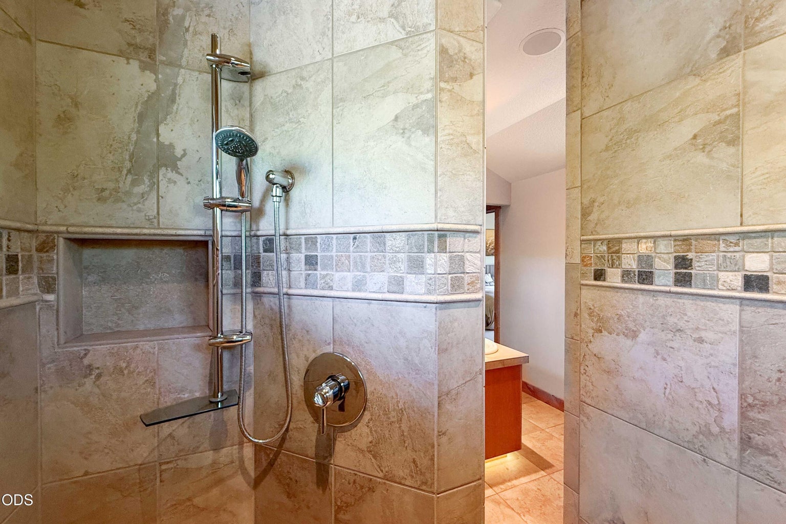 A second view of the tiled primary shower highlights the handheld shower system, built-in niche and substantial tilework designed for both comfort and easy daily use.