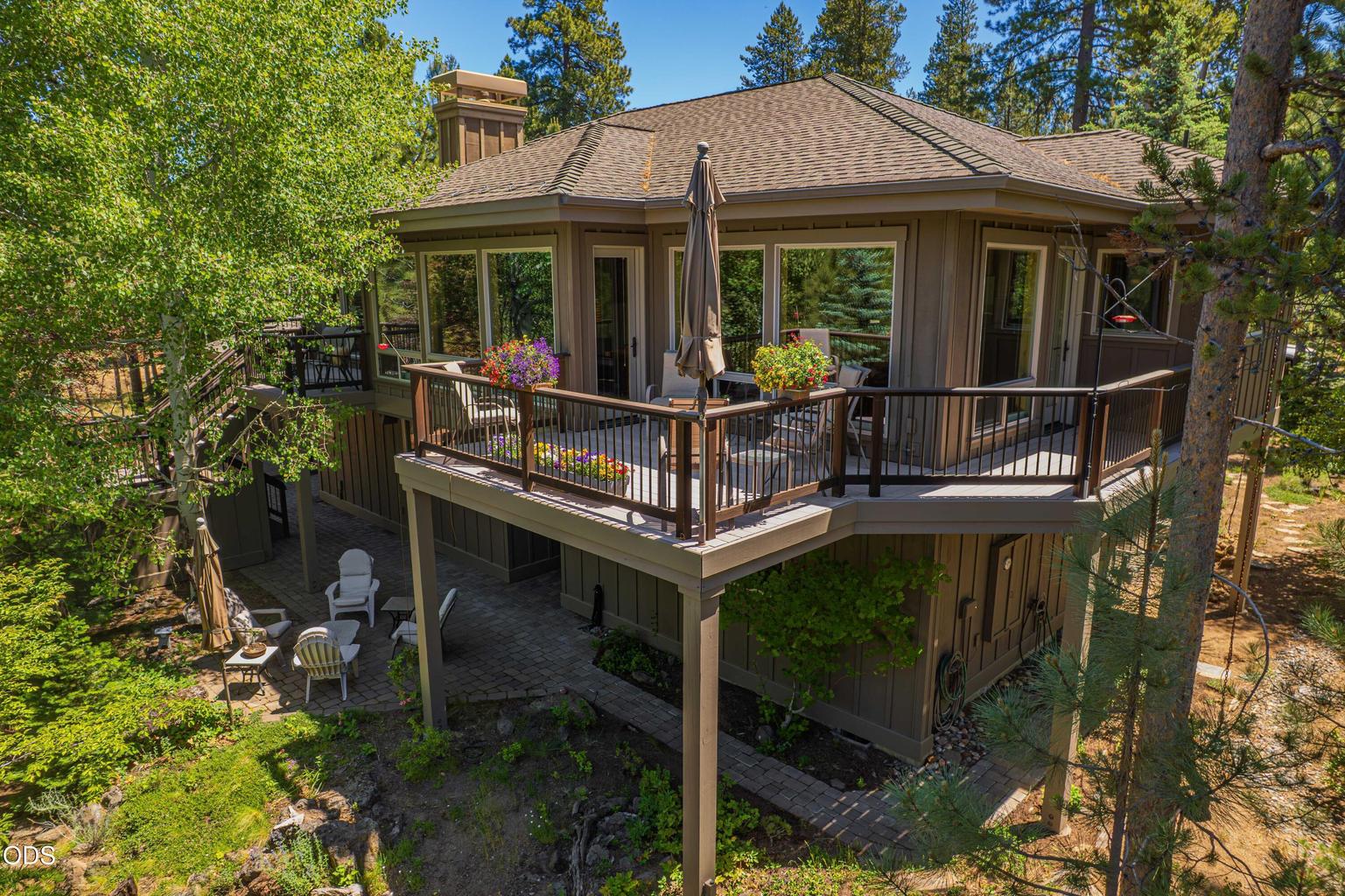 This rear exterior view reveals the home’s layered outdoor living spaces, including the wraparound deck serving the dining and kitchen areas, the separate deck adjoining the primary suite, lower patios and connecting exterior stairs. Surrounded by mature trees, the architecture is carefully integrated into the extraordinary Sunriver forest setting.